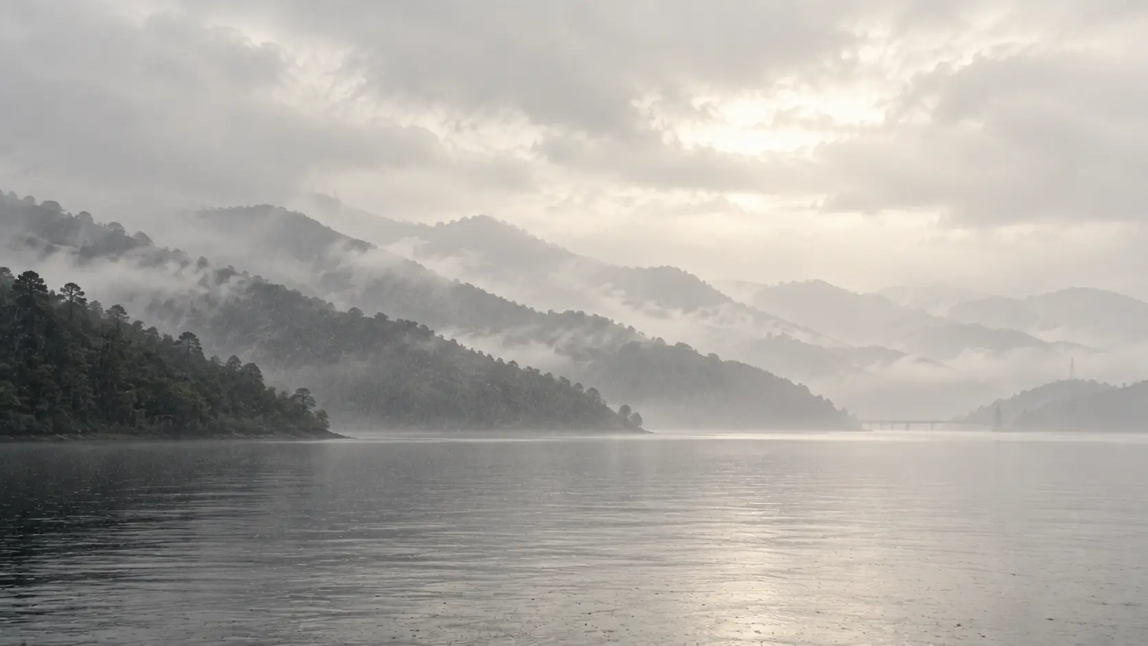 層疊的森林山脊消融於細雨之中，下方是一片銀灰色靜水